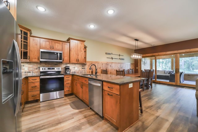 kitchen with decorative light fixtures, appliances with stainless steel finishes, dark stone countertops, and kitchen peninsula