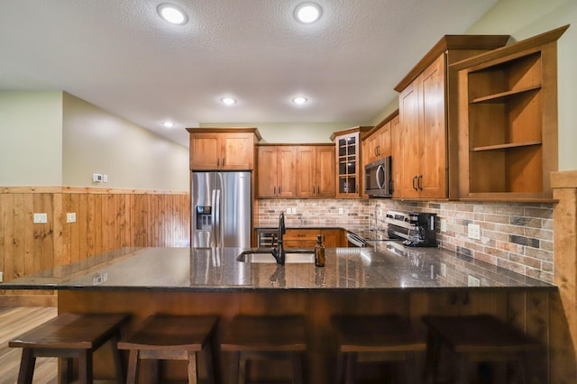 kitchen with glass insert cabinets, a sink, dark stone counters, brown cabinetry, and appliances with stainless steel finishes