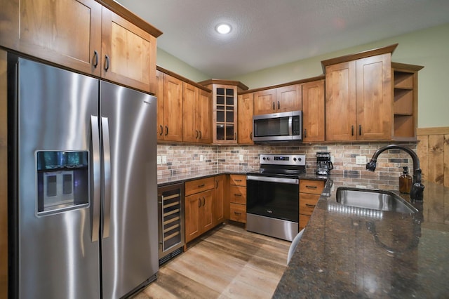 kitchen featuring a textured ceiling, beverage cooler, stainless steel appliances, sink, and dark stone countertops