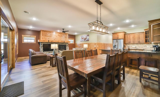 dining area featuring ceiling fan, sink, a stone fireplace, and hardwood / wood-style flooring