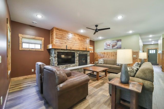 living room featuring a fireplace, hardwood / wood-style floors, ceiling fan, and wooden walls