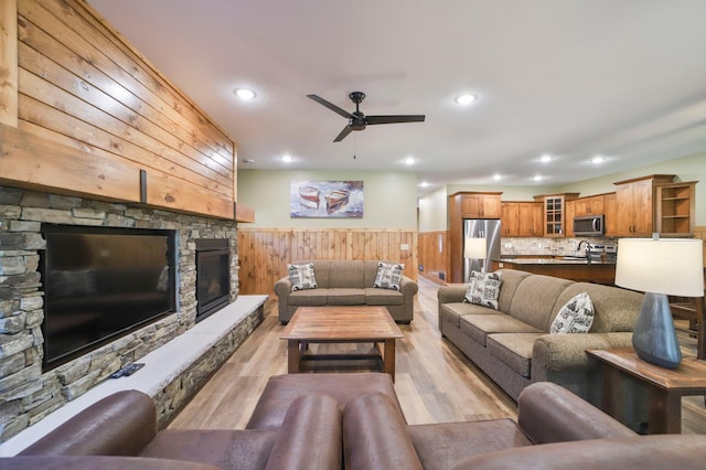 living room with sink, ceiling fan, light hardwood / wood-style floors, and a stone fireplace