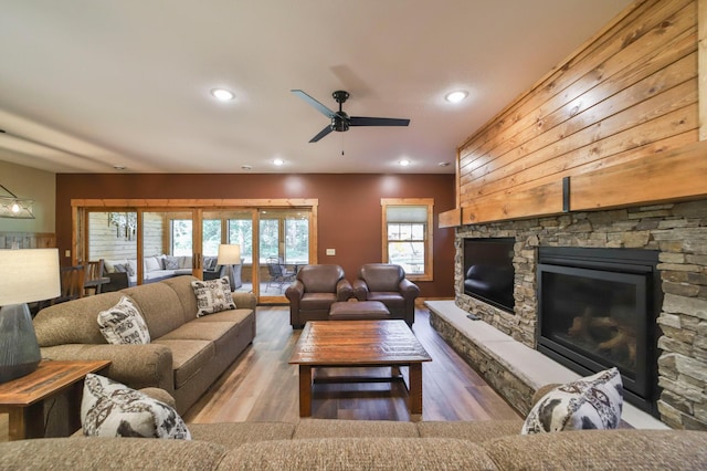 living room with wood-type flooring, ceiling fan, and a stone fireplace