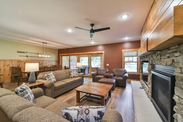 living room featuring light hardwood / wood-style flooring, wood walls, ceiling fan with notable chandelier, and a fireplace