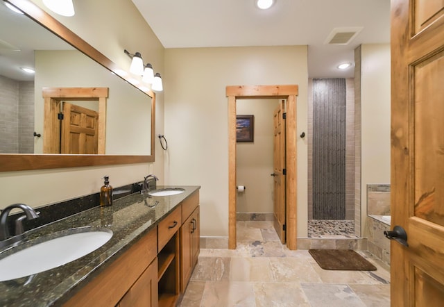 full bathroom featuring a sink, stone tile floors, a shower stall, and visible vents