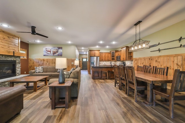 living room with dark hardwood / wood-style floors, wood walls, ceiling fan, and a stone fireplace