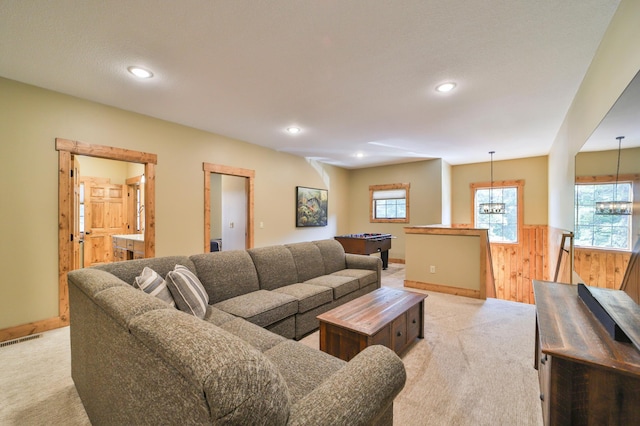 living room featuring light carpet, wood walls, and a notable chandelier