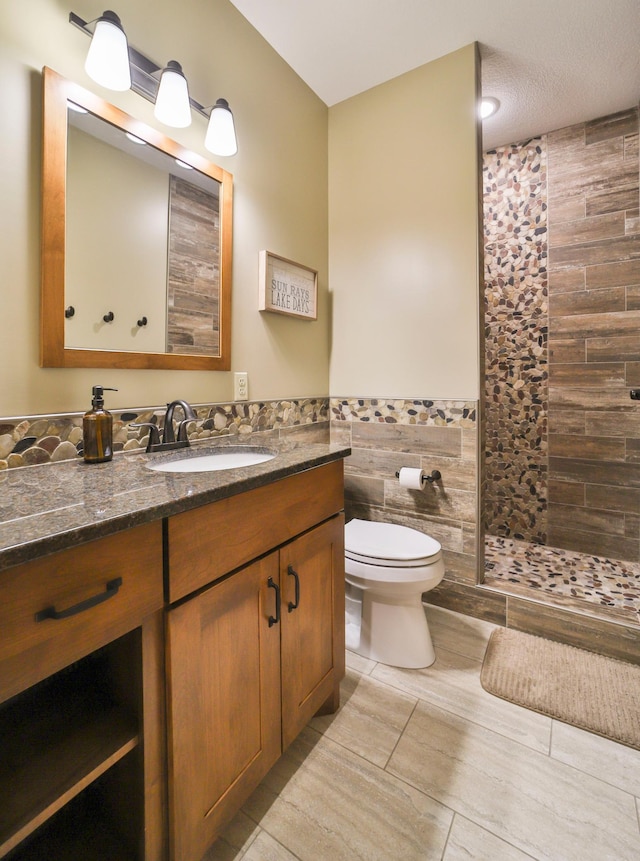 bathroom featuring vanity, toilet, a shower, and tile walls