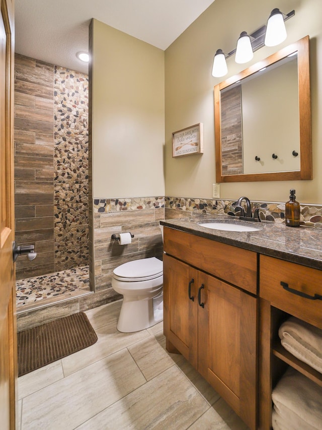 bathroom with toilet, tile patterned floors, vanity, a shower, and tile walls