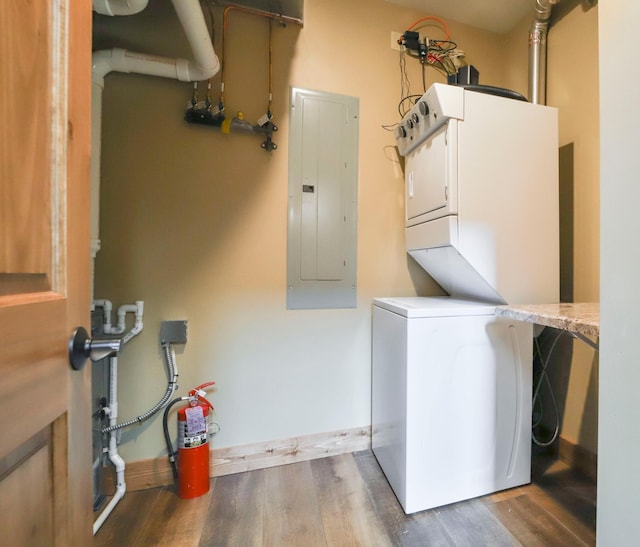 laundry area featuring electric panel, wood finished floors, laundry area, stacked washer and clothes dryer, and baseboards
