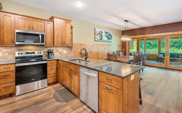 kitchen with light wood-type flooring, dark stone counters, kitchen peninsula, sink, and appliances with stainless steel finishes