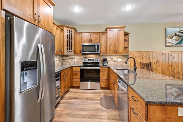 kitchen featuring backsplash, appliances with stainless steel finishes, light hardwood / wood-style floors, sink, and dark stone counters