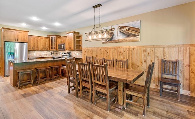 dining space with wood walls, sink, and light wood-type flooring