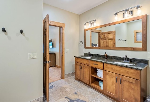 full bath featuring double vanity, baseboards, stone finish flooring, and a sink