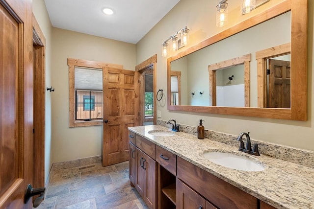 full bathroom with a sink, double vanity, baseboards, and stone finish floor