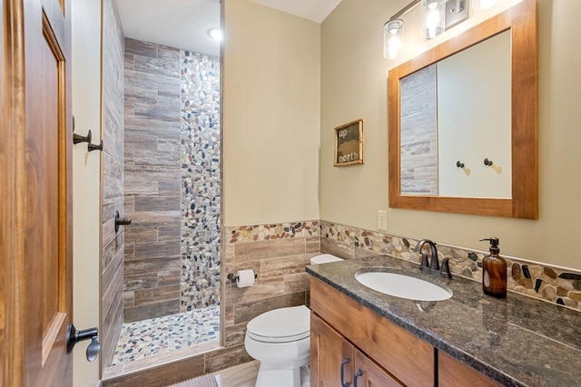 full bathroom with toilet, tile walls, vanity, wainscoting, and tiled shower