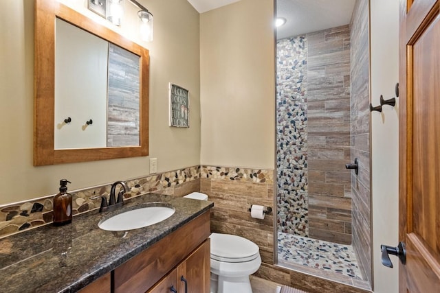 bathroom with vanity, toilet, a tile shower, and tile walls