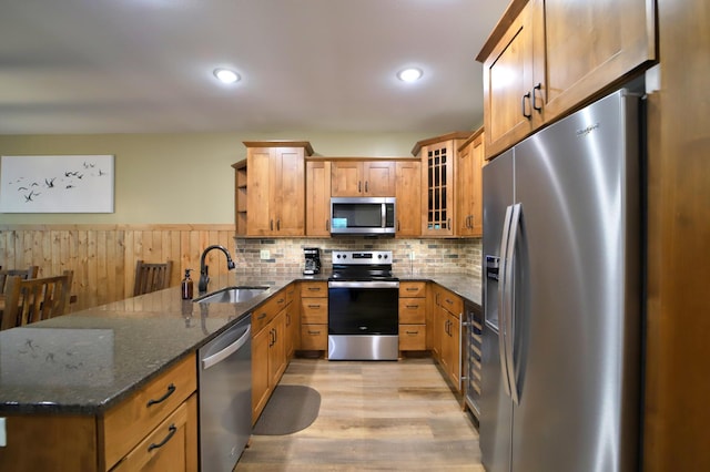 kitchen with appliances with stainless steel finishes, sink, decorative backsplash, light wood-type flooring, and dark stone counters