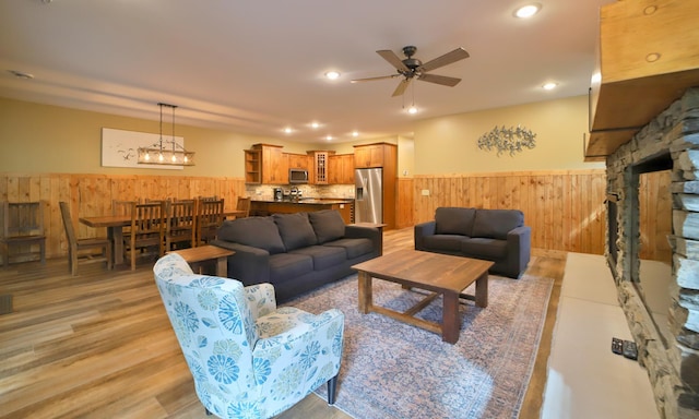 living room with ceiling fan with notable chandelier and light hardwood / wood-style flooring