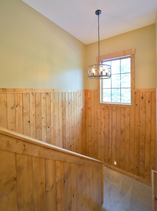 carpeted spare room featuring an inviting chandelier and wooden walls