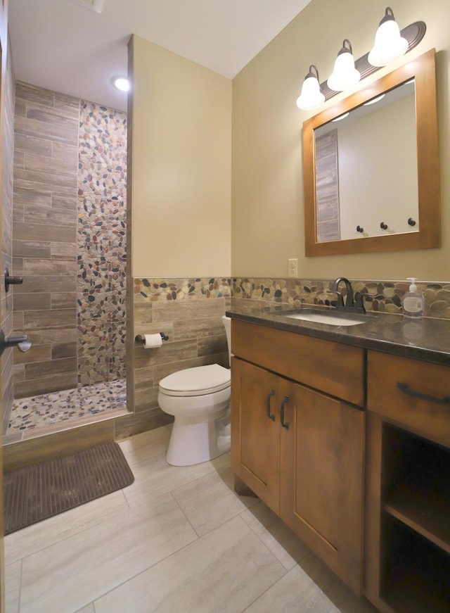 bathroom with toilet, tile patterned floors, vanity, a shower, and tile walls