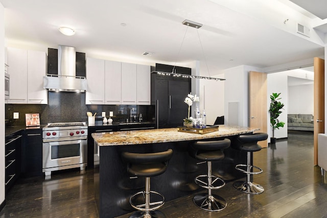 kitchen with a center island, wall chimney range hood, dark wood-type flooring, high quality appliances, and a breakfast bar