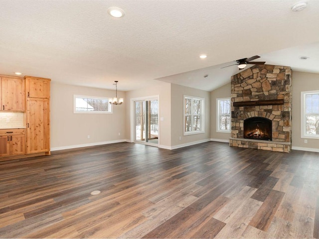 unfurnished living room featuring ceiling fan with notable chandelier, a wealth of natural light, lofted ceiling, and a stone fireplace