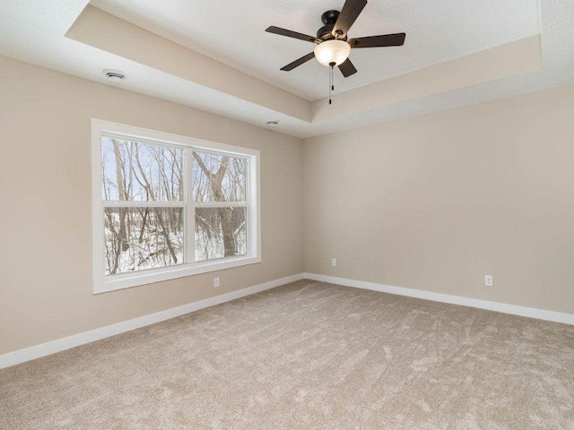 carpeted empty room featuring ceiling fan and a raised ceiling