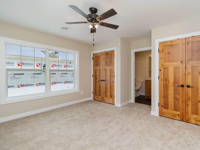 unfurnished bedroom with light carpet, ceiling fan, ensuite bathroom, and a textured ceiling