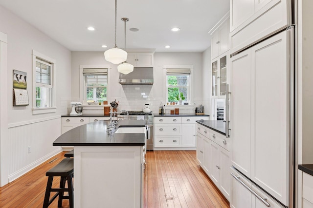 20390 Linwood Rd, Deephaven, MN 55331 - kitchen featuring premium appliances, dark countertops, exhaust hood, light wood-style flooring, and white cabinetry