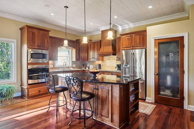 kitchen with appliances with stainless steel finishes, a center island, pendant lighting, and dark stone counters