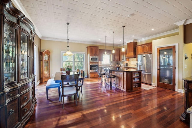 kitchen with dark wood-type flooring, hanging light fixtures, ornamental molding, a kitchen island, and stainless steel appliances