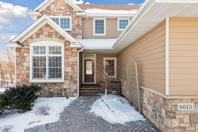 snow covered property entrance with stone siding and roof with shingles