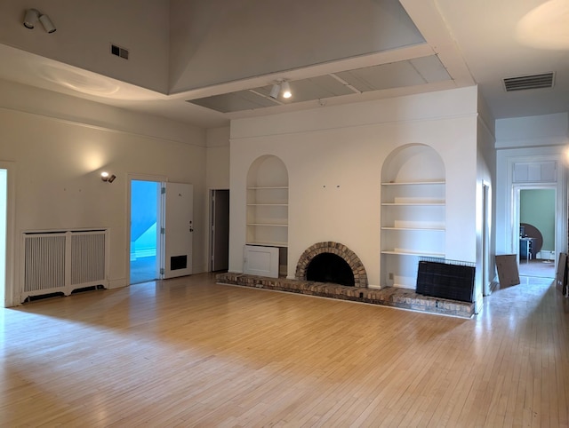 unfurnished living room featuring a towering ceiling, a fireplace, built in features, and light hardwood / wood-style flooring