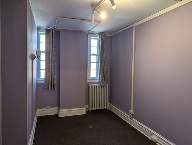 unfurnished room with radiator, dark colored carpet, and rail lighting