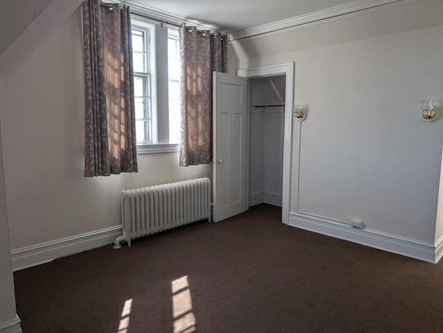 unfurnished bedroom featuring vaulted ceiling, a closet, dark colored carpet, and radiator heating unit