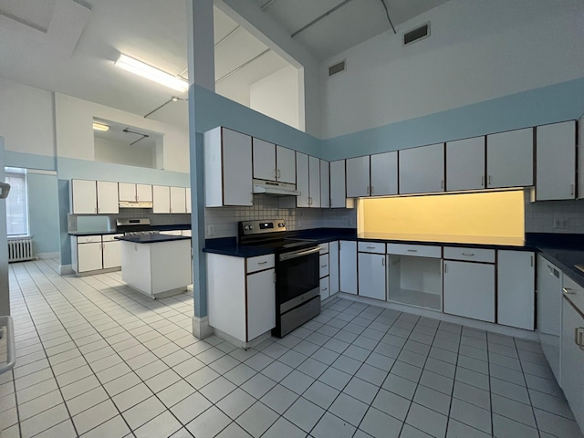 kitchen featuring a center island, a towering ceiling, light tile patterned floors, and range with electric stovetop