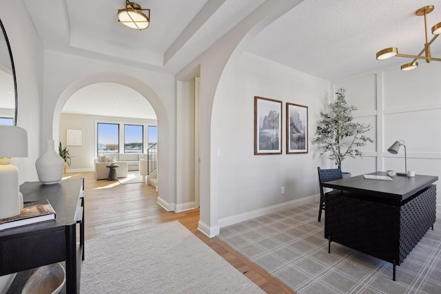 office with a textured ceiling, hardwood / wood-style flooring, an inviting chandelier, and a tray ceiling