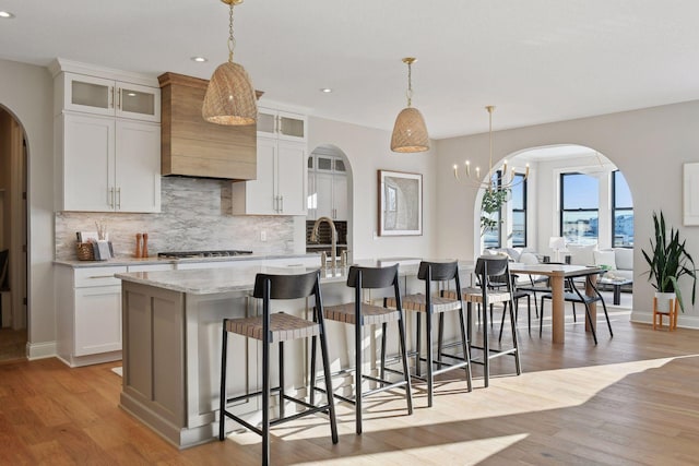 kitchen with custom exhaust hood, white cabinetry, a kitchen island with sink, and hanging light fixtures