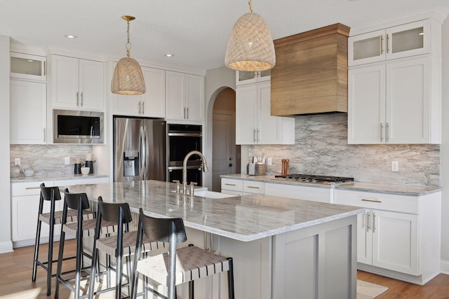 kitchen featuring appliances with stainless steel finishes, white cabinetry, decorative light fixtures, and a kitchen island with sink