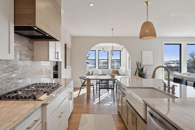 kitchen with custom exhaust hood, pendant lighting, stainless steel appliances, a notable chandelier, and tasteful backsplash