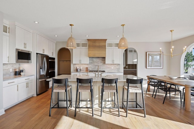 kitchen featuring a center island with sink, white cabinetry, hanging light fixtures, and appliances with stainless steel finishes