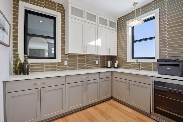 kitchen with pendant lighting, light wood-type flooring, wine cooler, gray cabinetry, and white cabinets