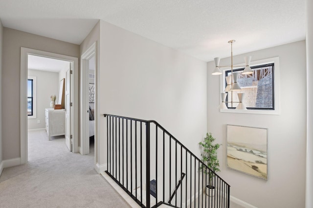 hallway with a textured ceiling, a chandelier, and light colored carpet