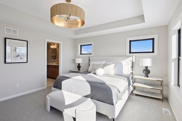 bedroom featuring connected bathroom, a raised ceiling, and carpet flooring