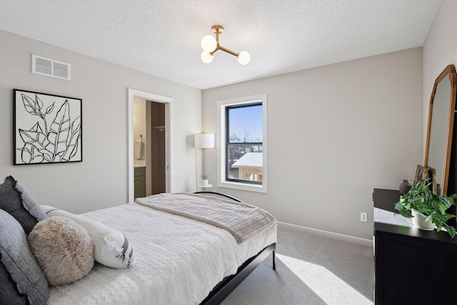 carpeted bedroom with ensuite bath and a textured ceiling