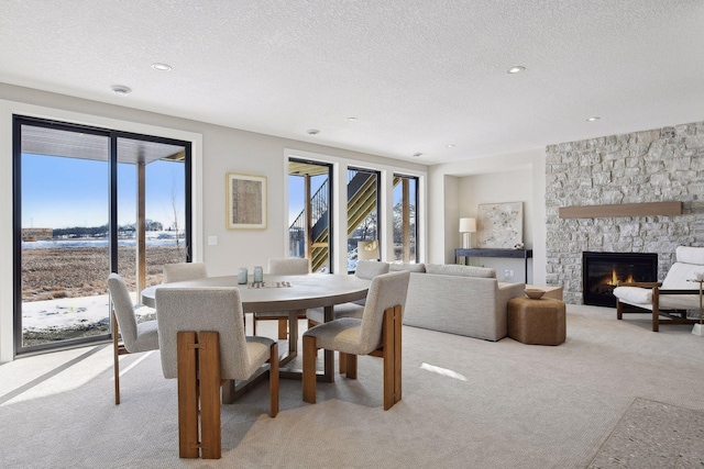 dining room with a textured ceiling, light carpet, and a stone fireplace