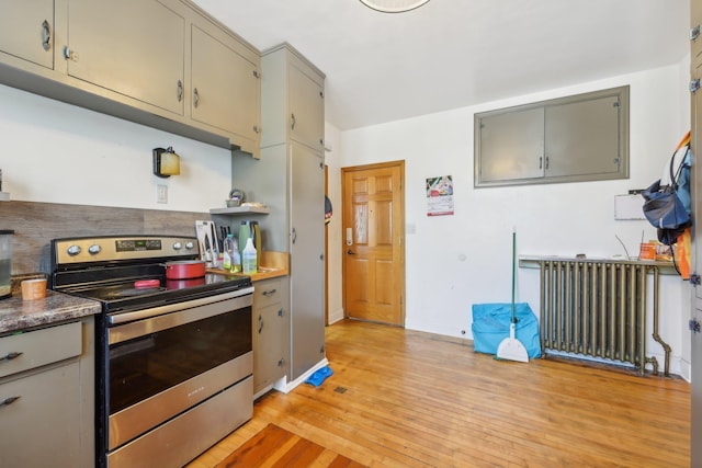 kitchen with gray cabinetry, light wood-type flooring, stainless steel electric range oven, and radiator