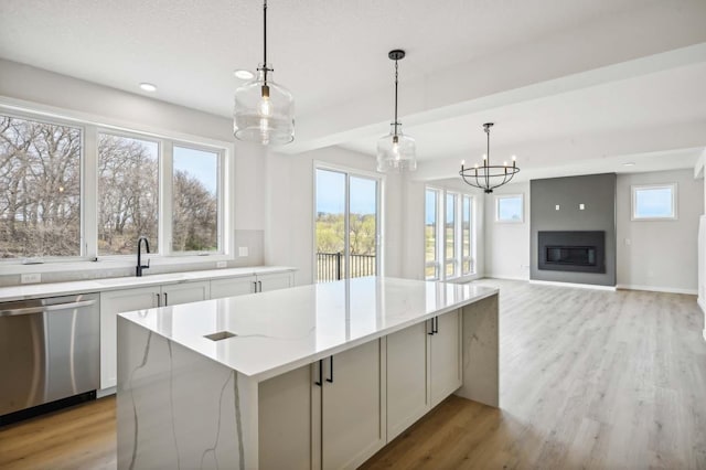 kitchen featuring dishwasher, sink, a center island, light stone counters, and light hardwood / wood-style flooring