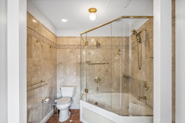 bathroom with tile patterned floors, toilet, shower / bath combination with glass door, and tile walls